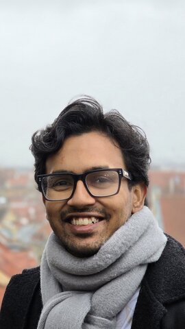 Naeratav mees prillide ja salliga, taustal linnapilt kirikuga.