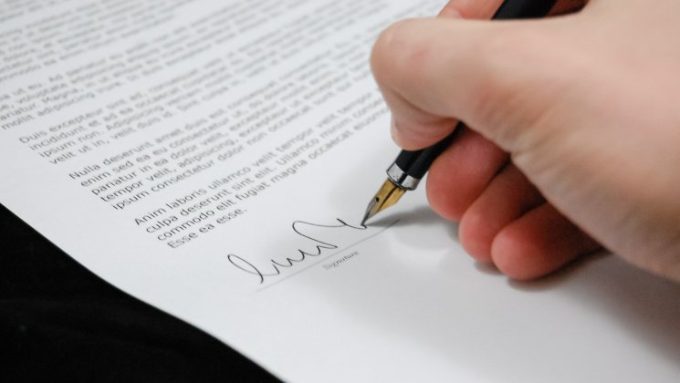Käsi kirjutab pastakaga paberile allkirja.